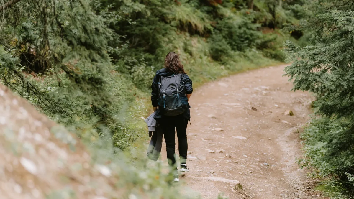 Hiker with a backpack walking along a dirt trail through forest in Banff