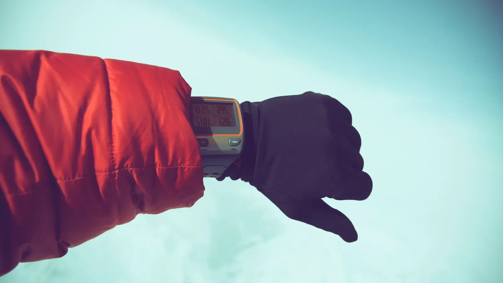 Gloved hand wearing an outdoor digital watch against a snowy background
