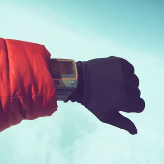Gloved hand wearing an outdoor digital watch against a snowy background