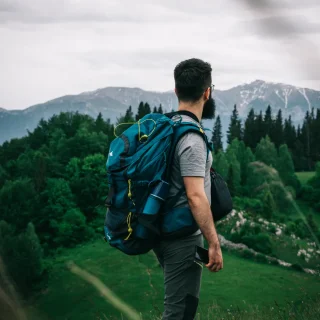 Hiker with a blue backpack looking out over forested mountains