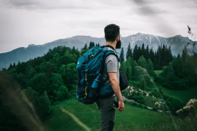Hiker with a blue backpack looking out over forested mountains
