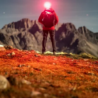 Hiker with a lit headlamp facing a mountain landscape at dusk