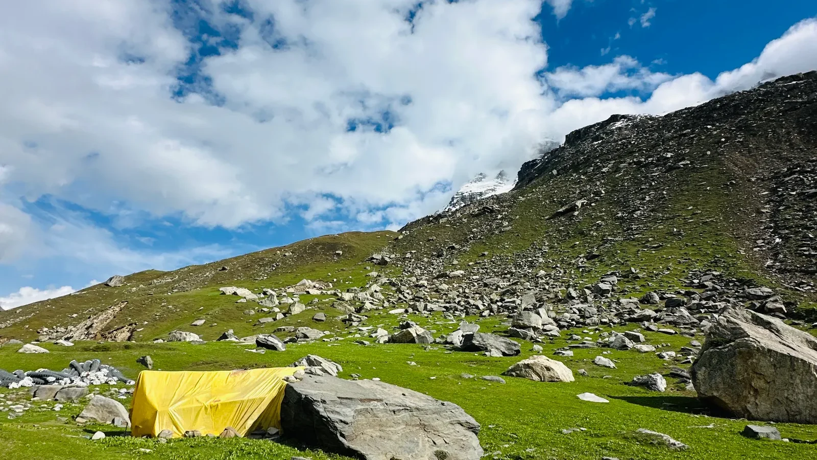 Yellow backpacking tent pitched in an alpine meadow under a blue sky