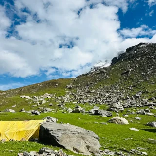 Yellow backpacking tent pitched in an alpine meadow under a blue sky