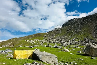 Yellow backpacking tent pitched in an alpine meadow under a blue sky
