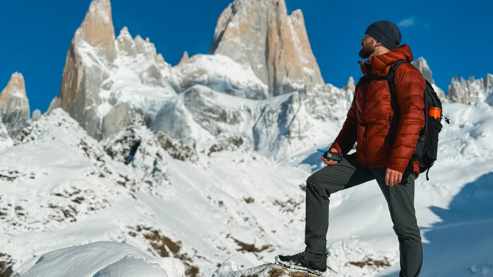 Hiker in a puffy insulated jacket standing in snow below jagged peaks