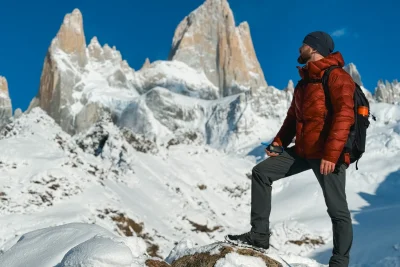 Hiker in a puffy insulated jacket standing in snow below jagged peaks