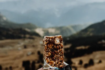Hand holding a cereal bar with a mountain landscape in the background