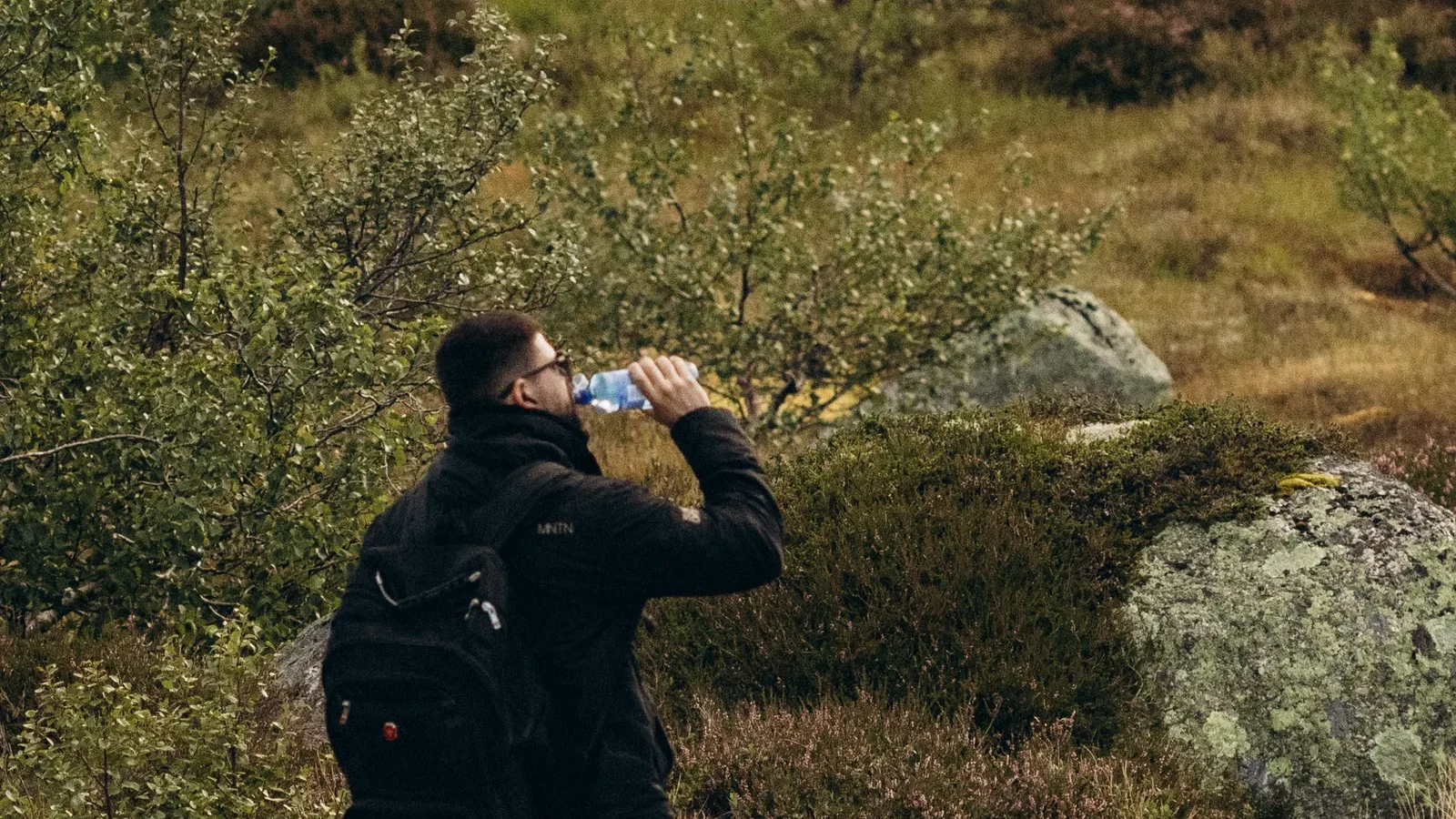 Hiker drinking water while resting on a mossy hillside in Norway