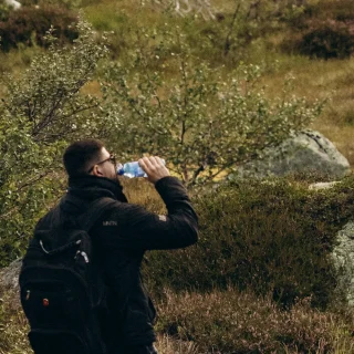Hiker drinking water while resting on a mossy hillside in Norway