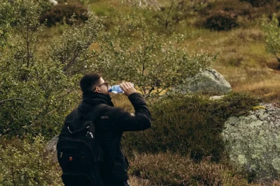 Hiker drinking water while resting on a mossy hillside in Norway