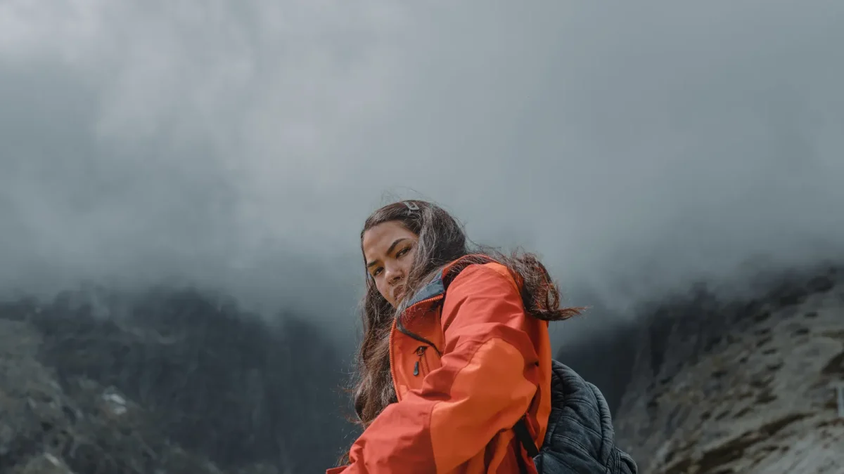 Hiker in an orange shell jacket on a foggy mountain trail