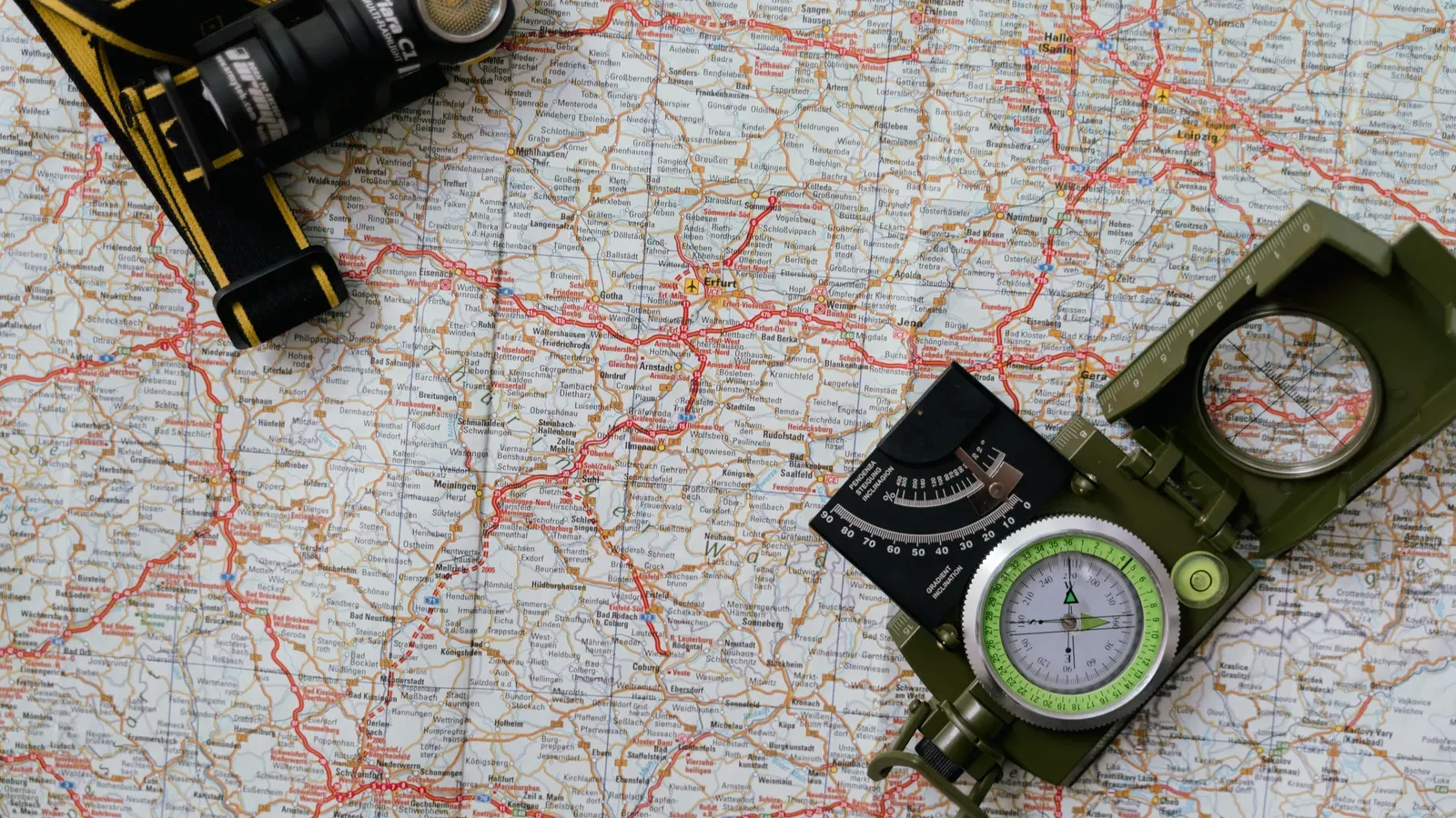 Overhead view of a paper map with a compass and a headlamp