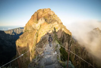 Hikers walking along a rocky mountain ridge path above the clouds at sunrise