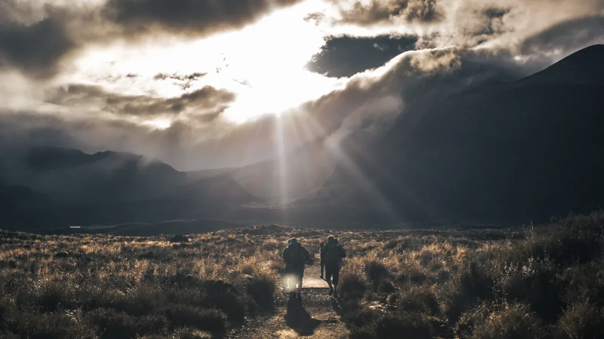 Two hikers crossing a high valley under dramatic storm clouds and low sunlight