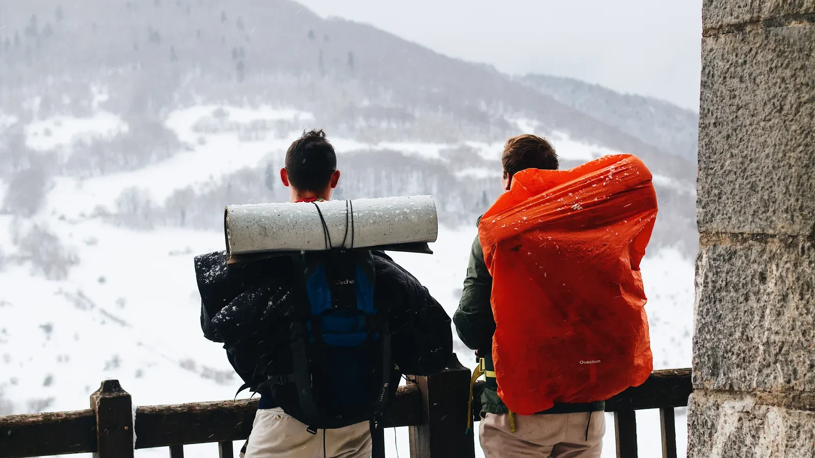 Two hikers with large backpacks looking at a snowy mountain view in winter