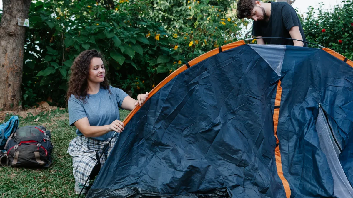 Two hikers pitching a two-person backpacking tent in a sunlit forest clearing