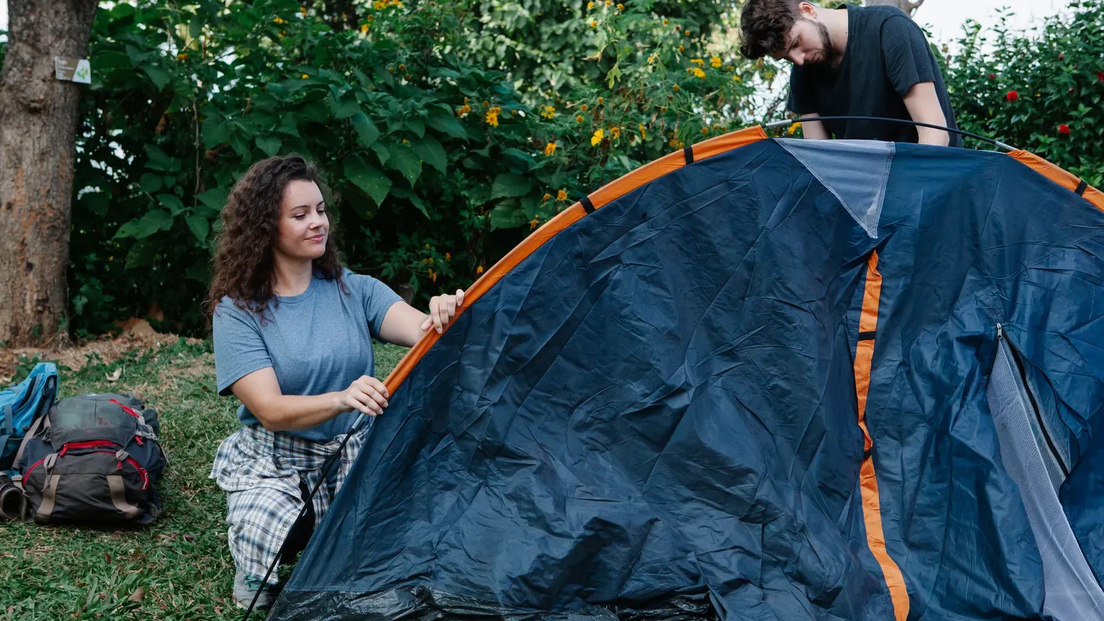 Two hikers pitching a two-person backpacking tent in a sunlit forest clearing