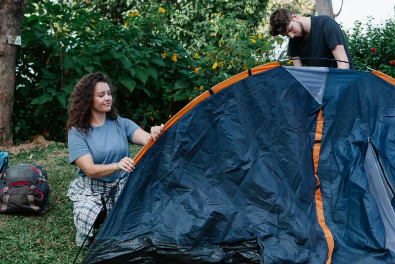Two hikers pitching a two-person backpacking tent in a sunlit forest clearing