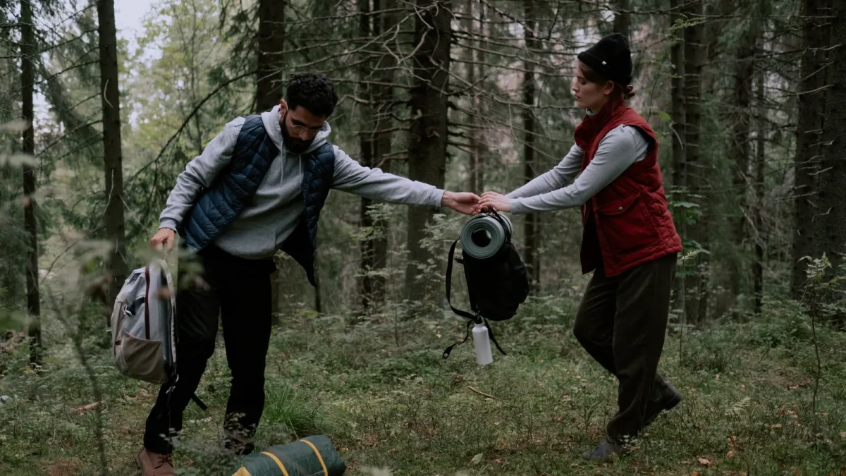 Two hikers passing a rolled tent piece to each other in the forest