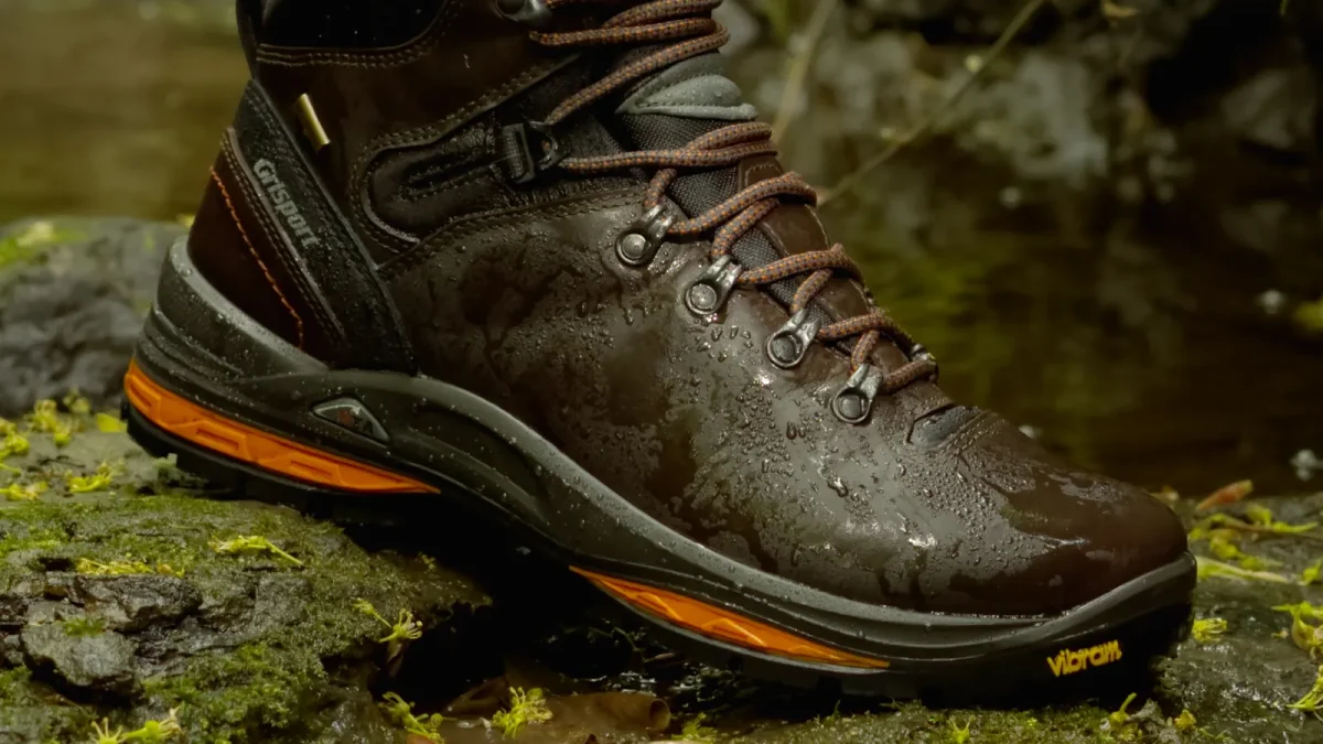 Hiking boot with a deep lugged sole gripping a wet, mossy rock