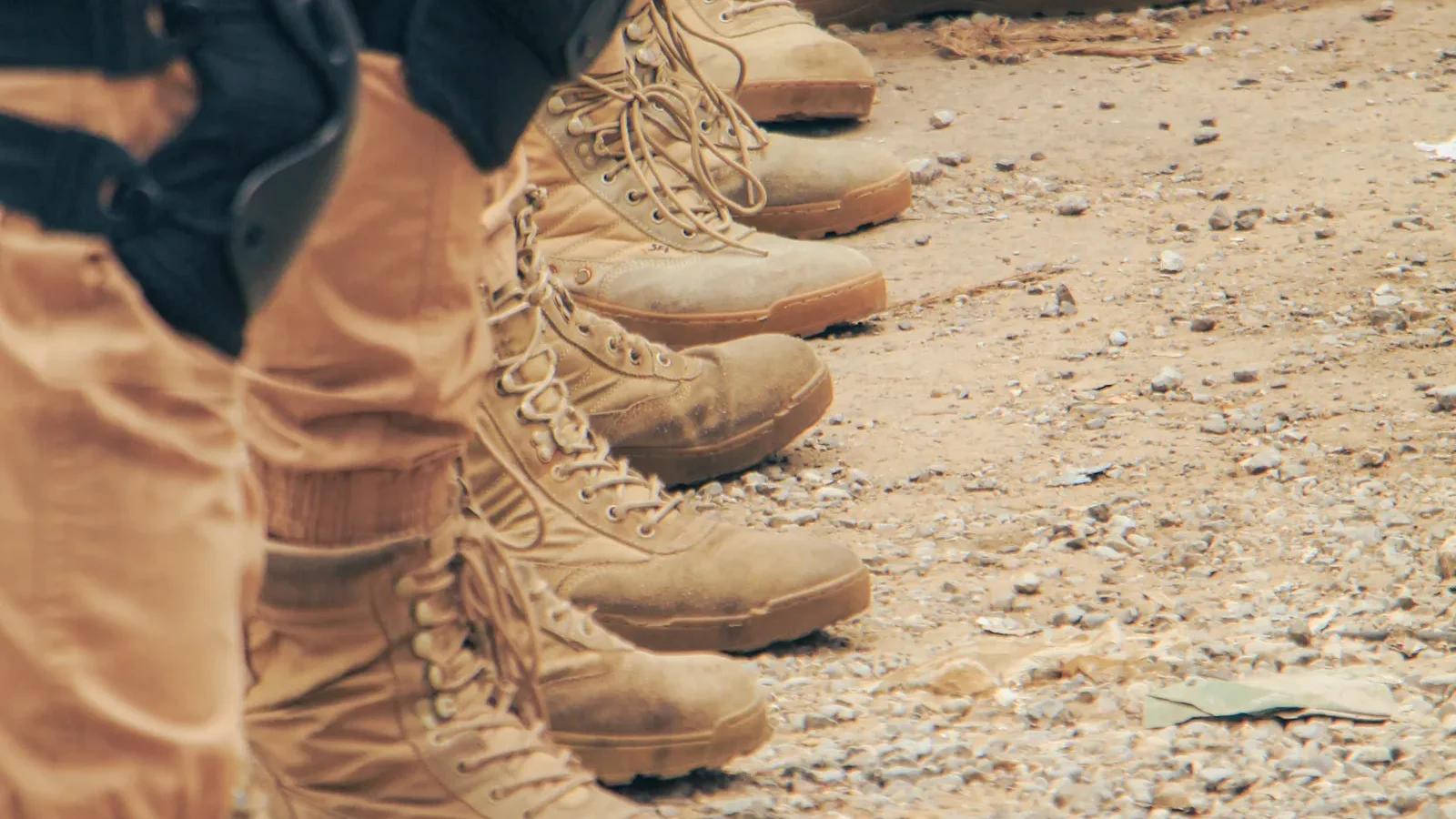 Row of tan military combat boots lined up on sandy ground