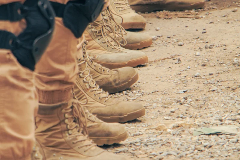 Row of tan military combat boots lined up on sandy ground