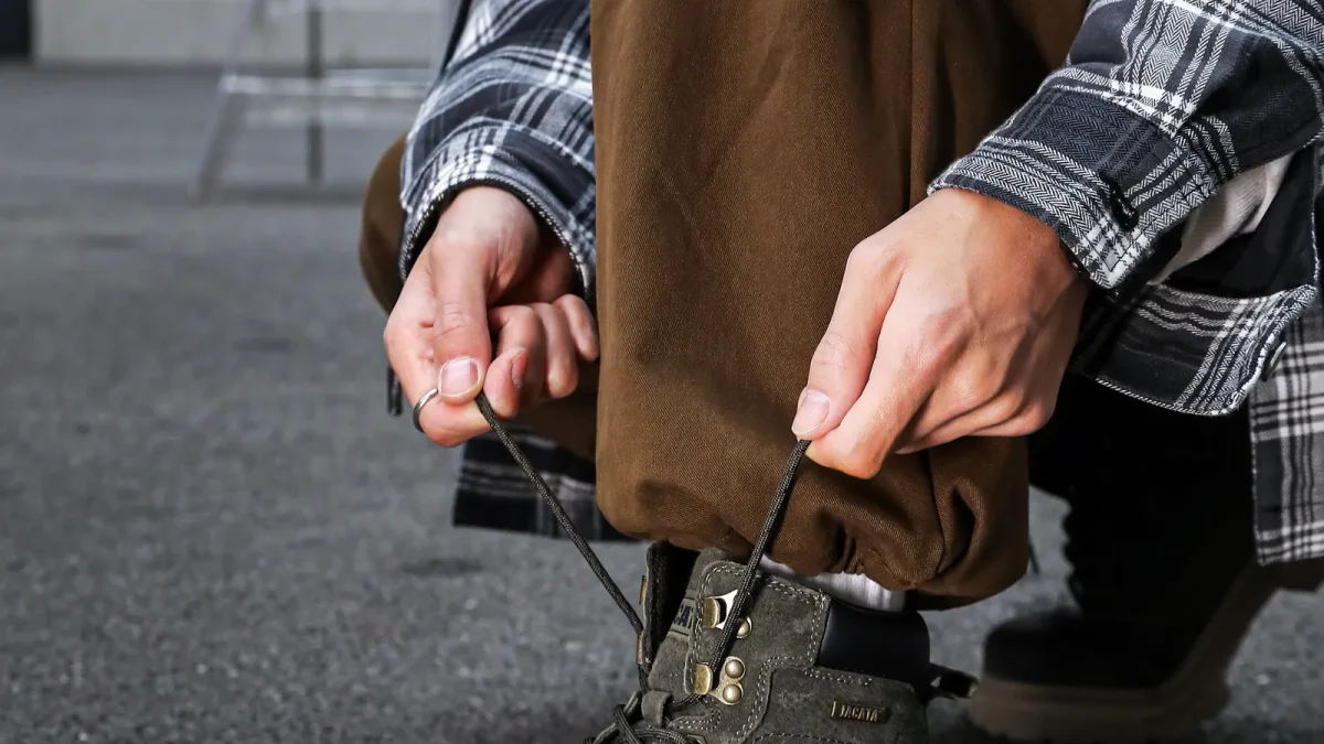 Person crouching to tie the laces of olive tactical boots on pavement
