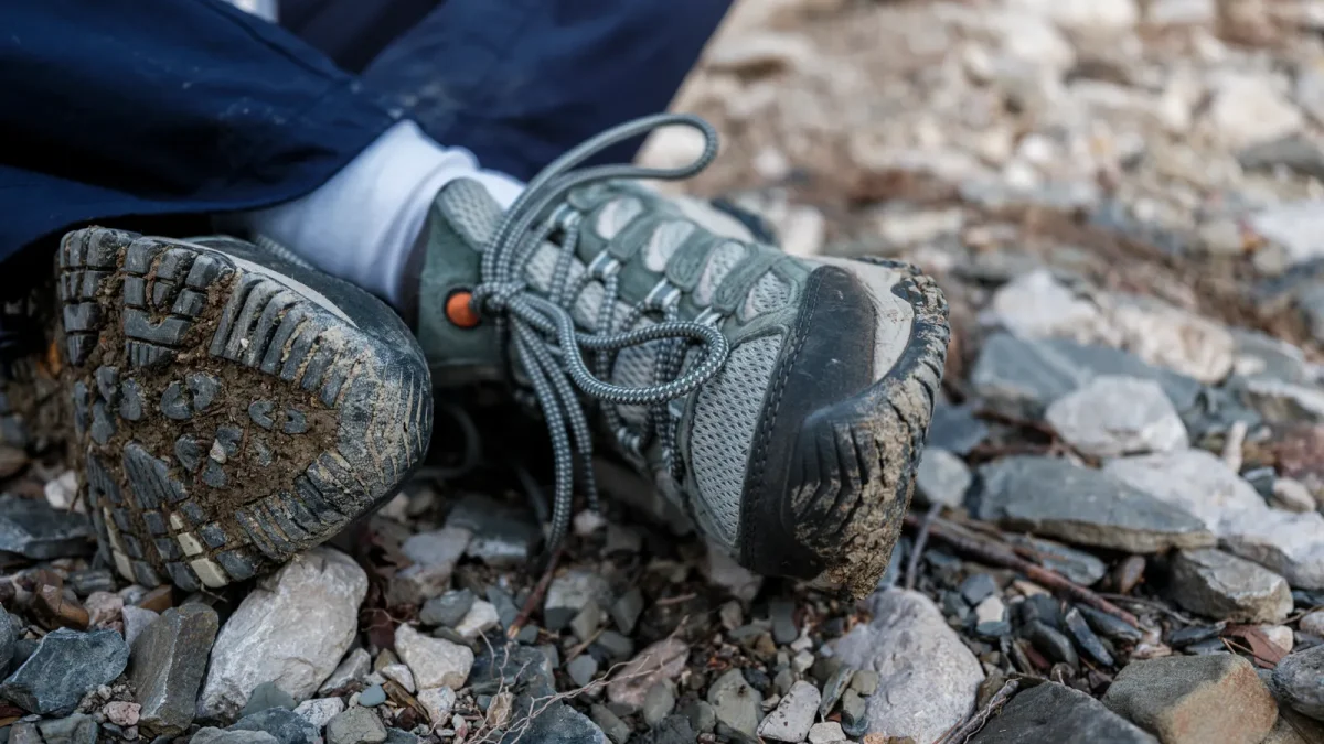 Mud-speckled hiking shoes with deep lugs resting on a rocky trail