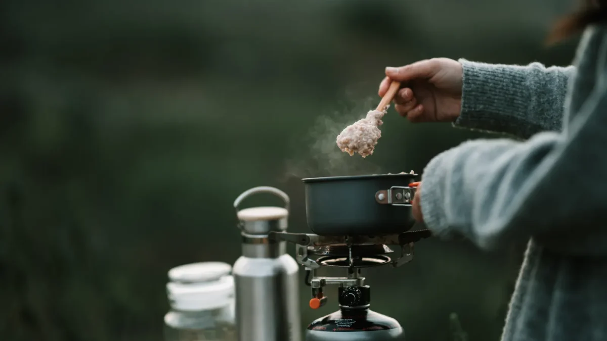 Camper adding food to a pot cooking on a portable stove outdoors