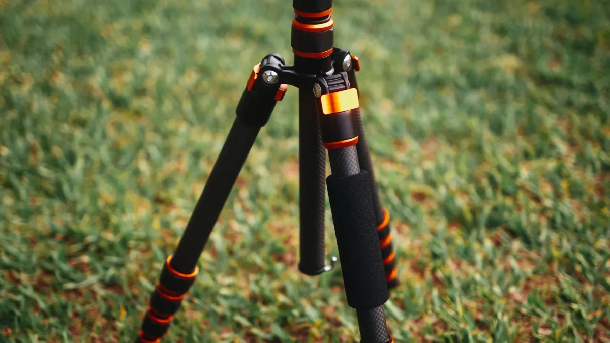 Close-up of an orange and black carbon fiber tripod on grass