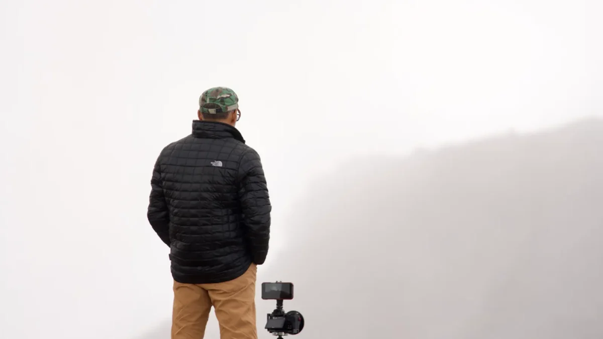 Hiker with a camera on a tripod overlooking a foggy mountain view