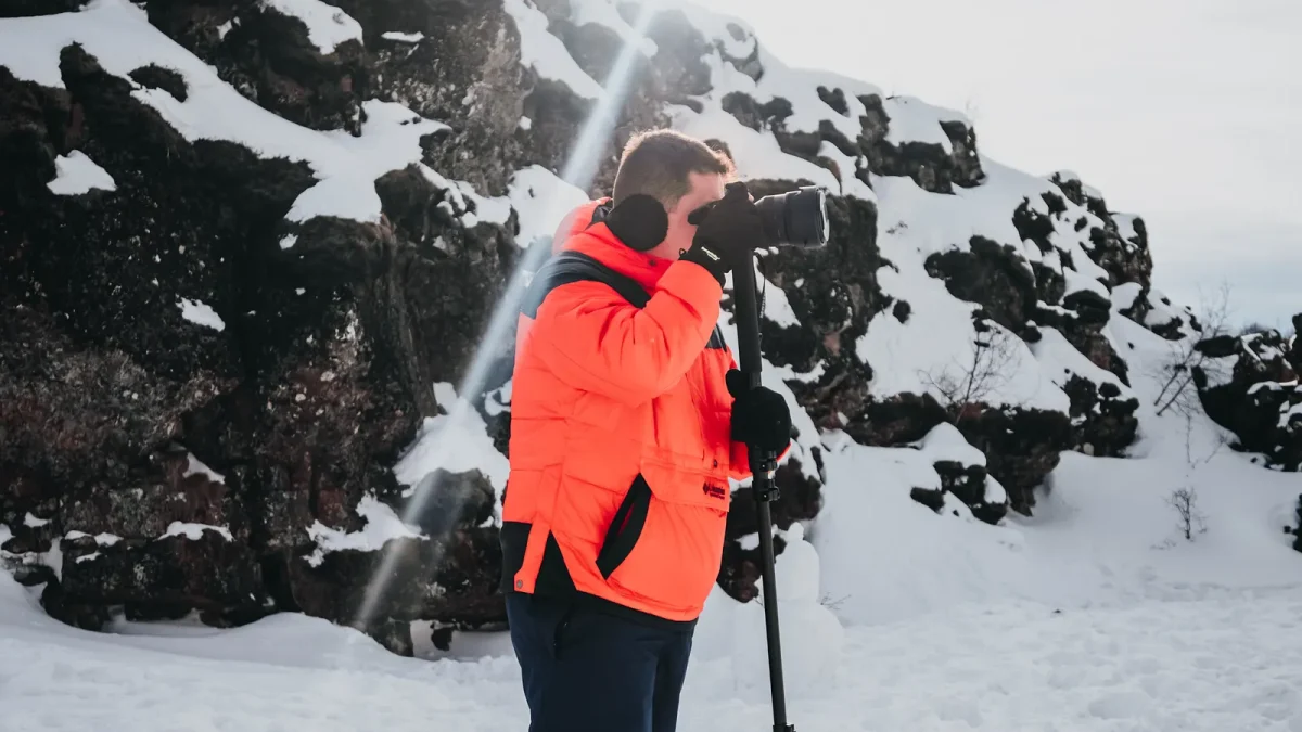 Photographer in an orange jacket using a tripod on a snowy slope