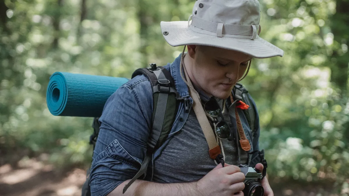 Hiker with a hat carrying a camera on a forest pathway