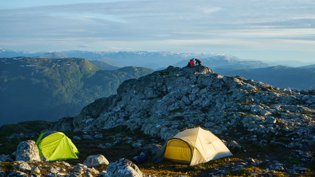Two backpacking tents, green and tan, pitched on a rocky mountain ridge