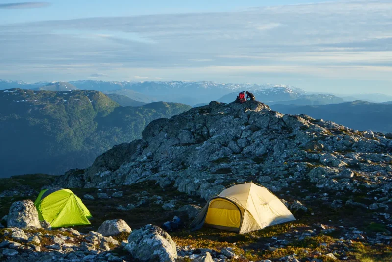 Two backpacking tents, green and tan, pitched on a rocky mountain ridge