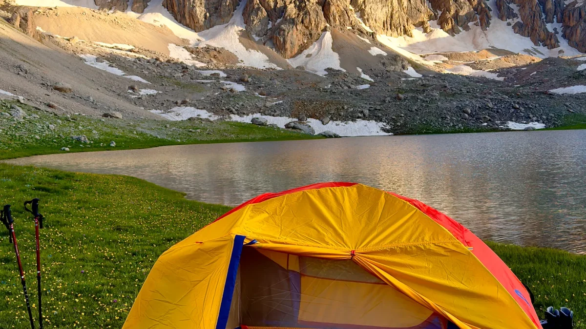 Orange and blue dome tent pitched on grass beside a mountain lake