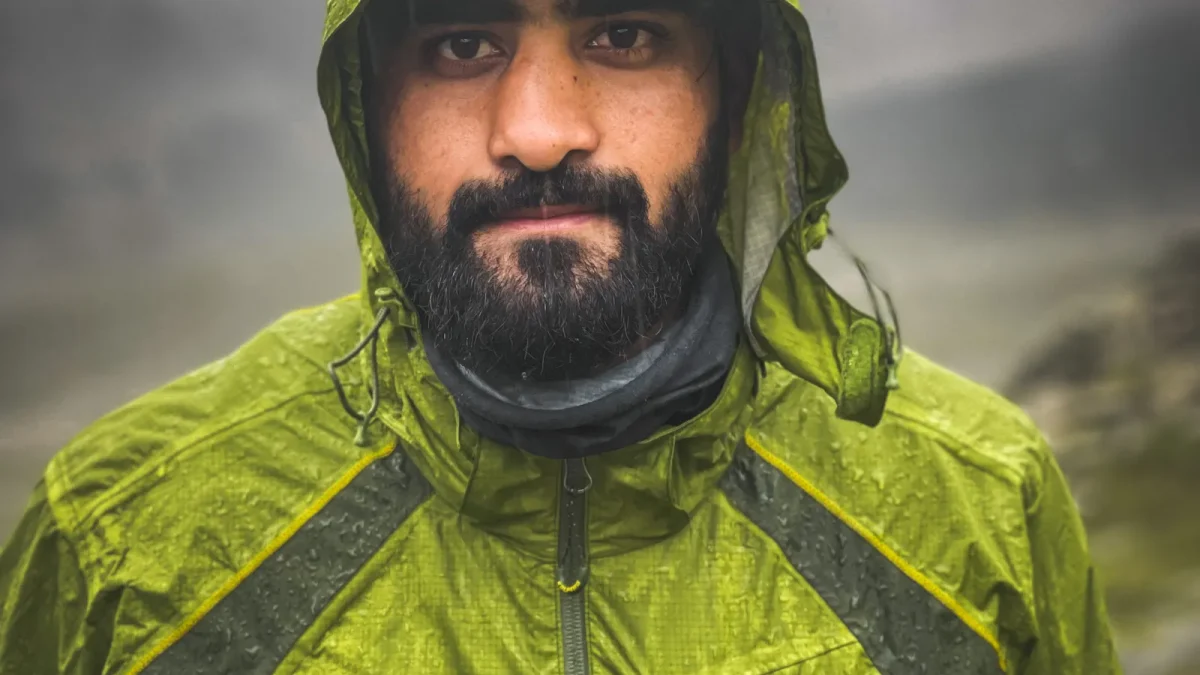 Bearded hiker wearing a green hooded rain jacket in misty weather