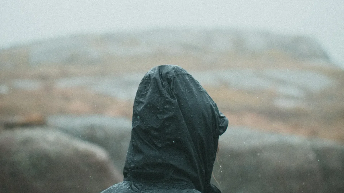 Hiker in a hooded jacket looking out over a fog-covered rocky landscape