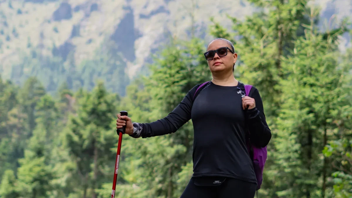 Woman hiking with a trekking pole through a lush mountain forest