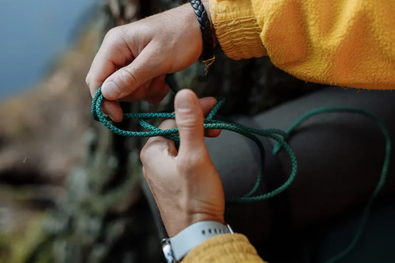 Hands tying a knot in a length of green cord outdoors