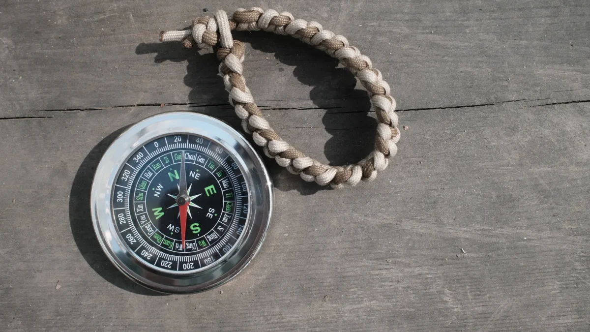Compass beside a braided tan paracord strap on a wooden surface