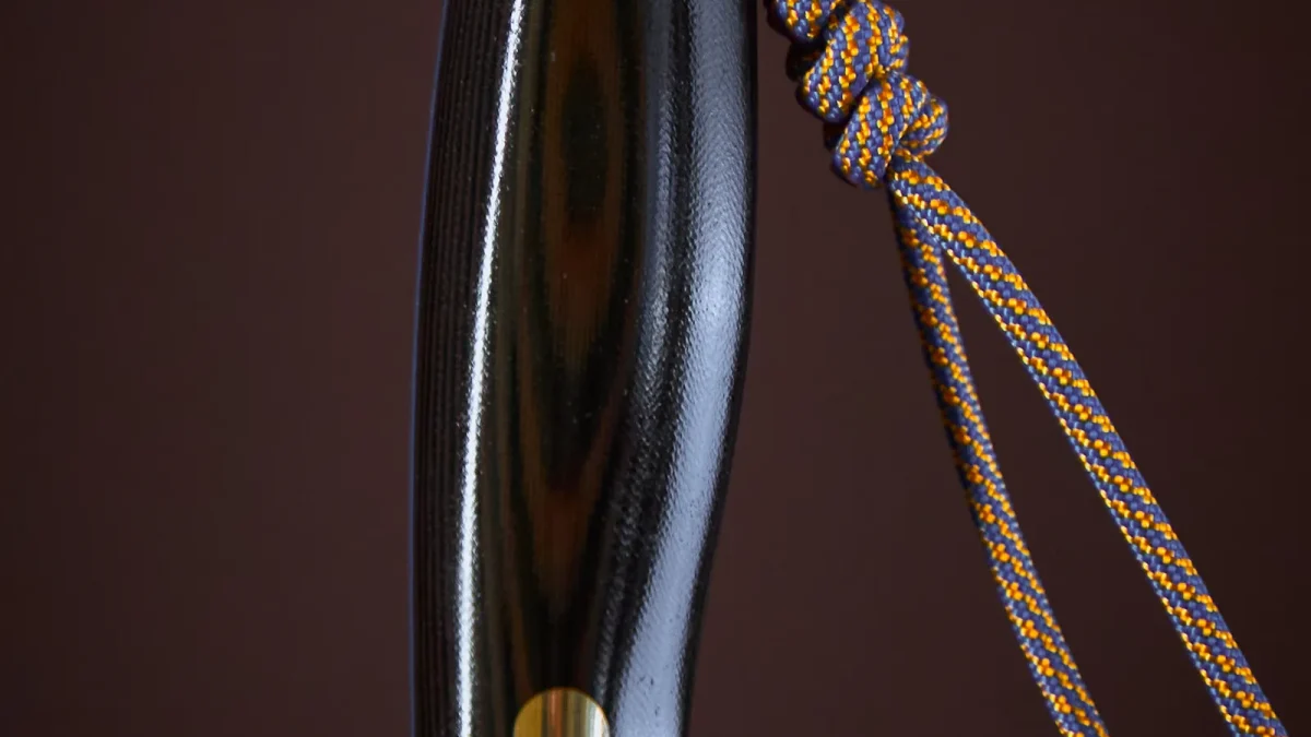 Knife handle with a knotted paracord lanyard against a dark background