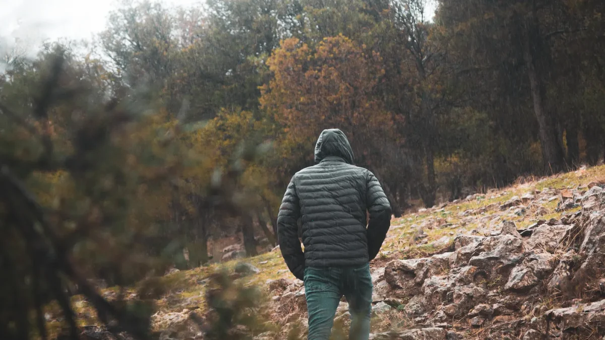 Hiker in a hooded jacket walking alone on a rocky forest trail