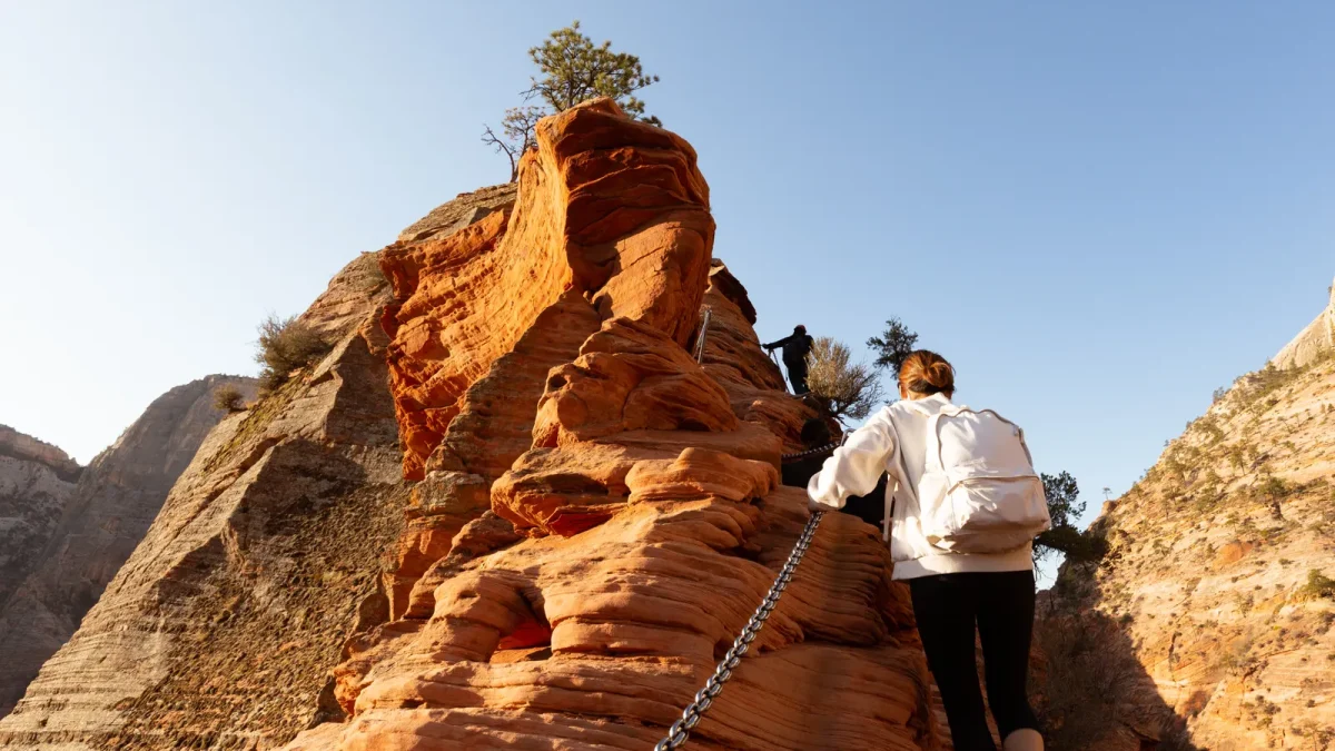 Hiker following a chain bolted into steep sandstone on a ridge trail