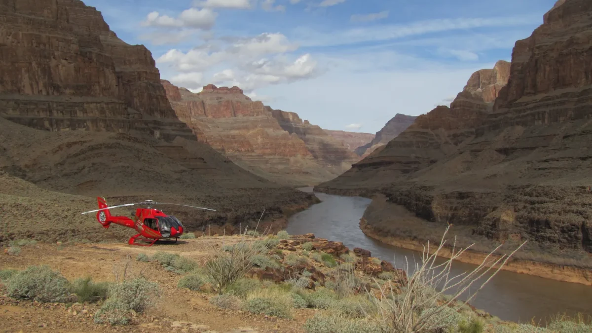 Red tour helicopter parked on a canyon rim above a river