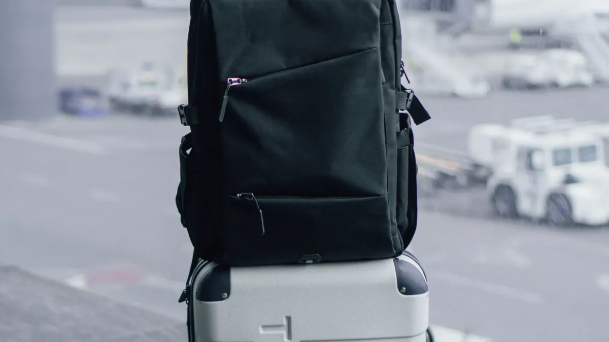 Black travel backpack sitting on top of a wheeled suitcase at an airport terminal