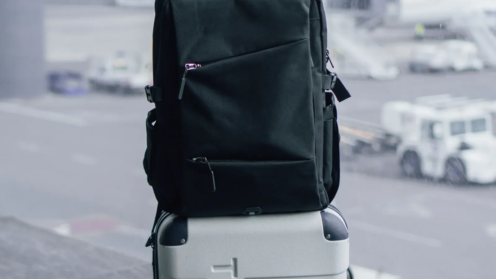 Black travel backpack sitting on top of a wheeled suitcase at an airport terminal