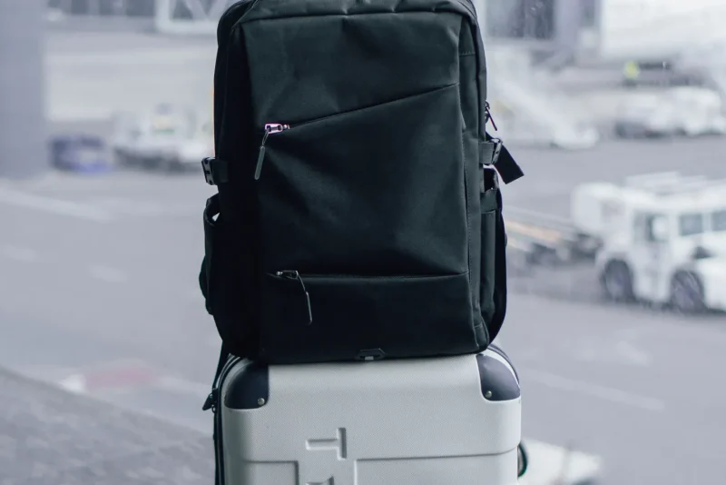 Black travel backpack sitting on top of a wheeled suitcase at an airport terminal