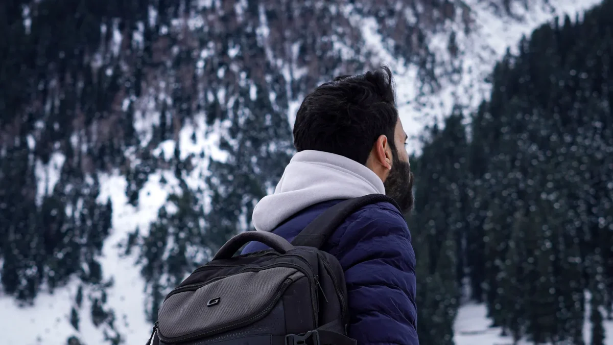 Man wearing a backpack looking out over a snowy mountain forest